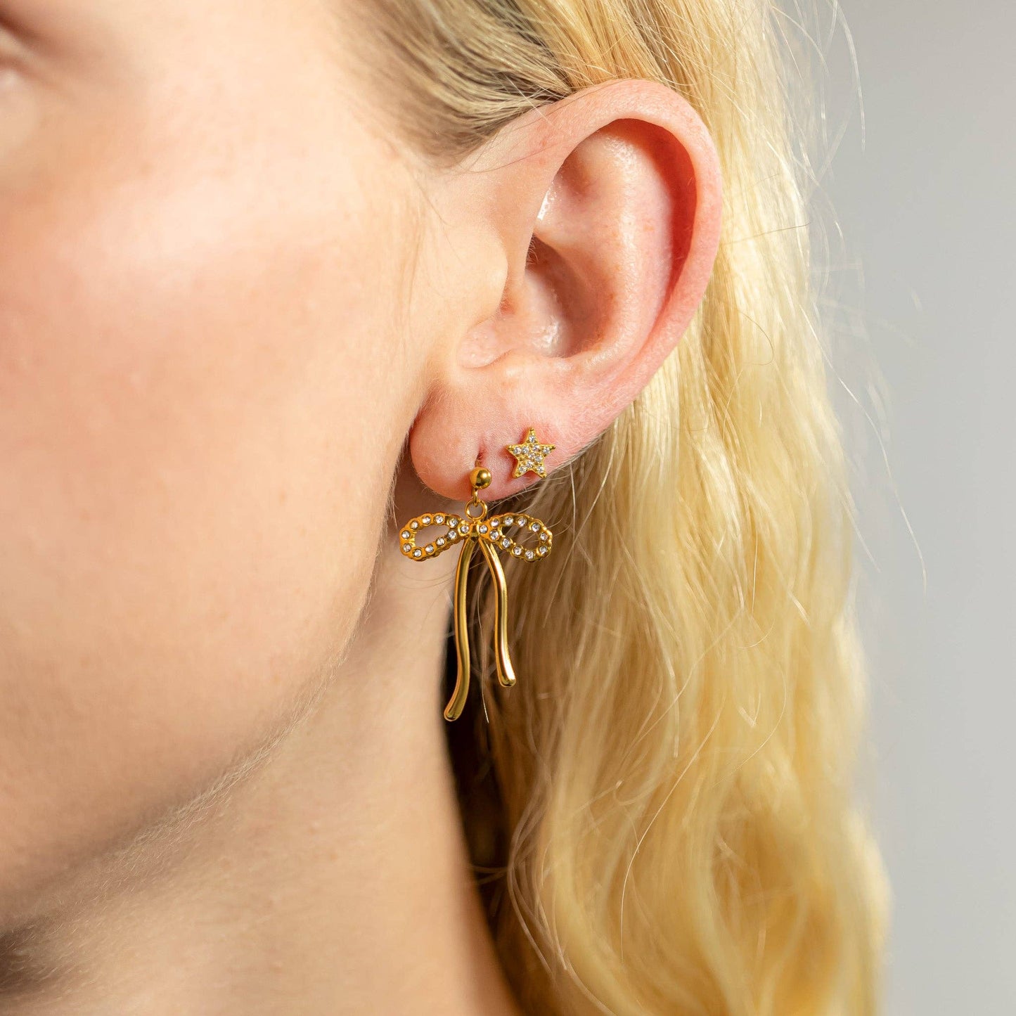 Close-up of a person wearing gold bow-shaped earrings with a blurred background