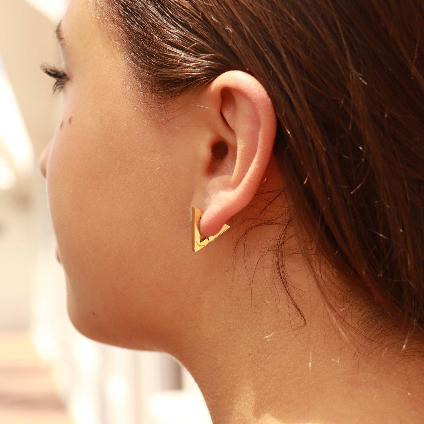 Close-up of a person wearing a gold triangle earring.