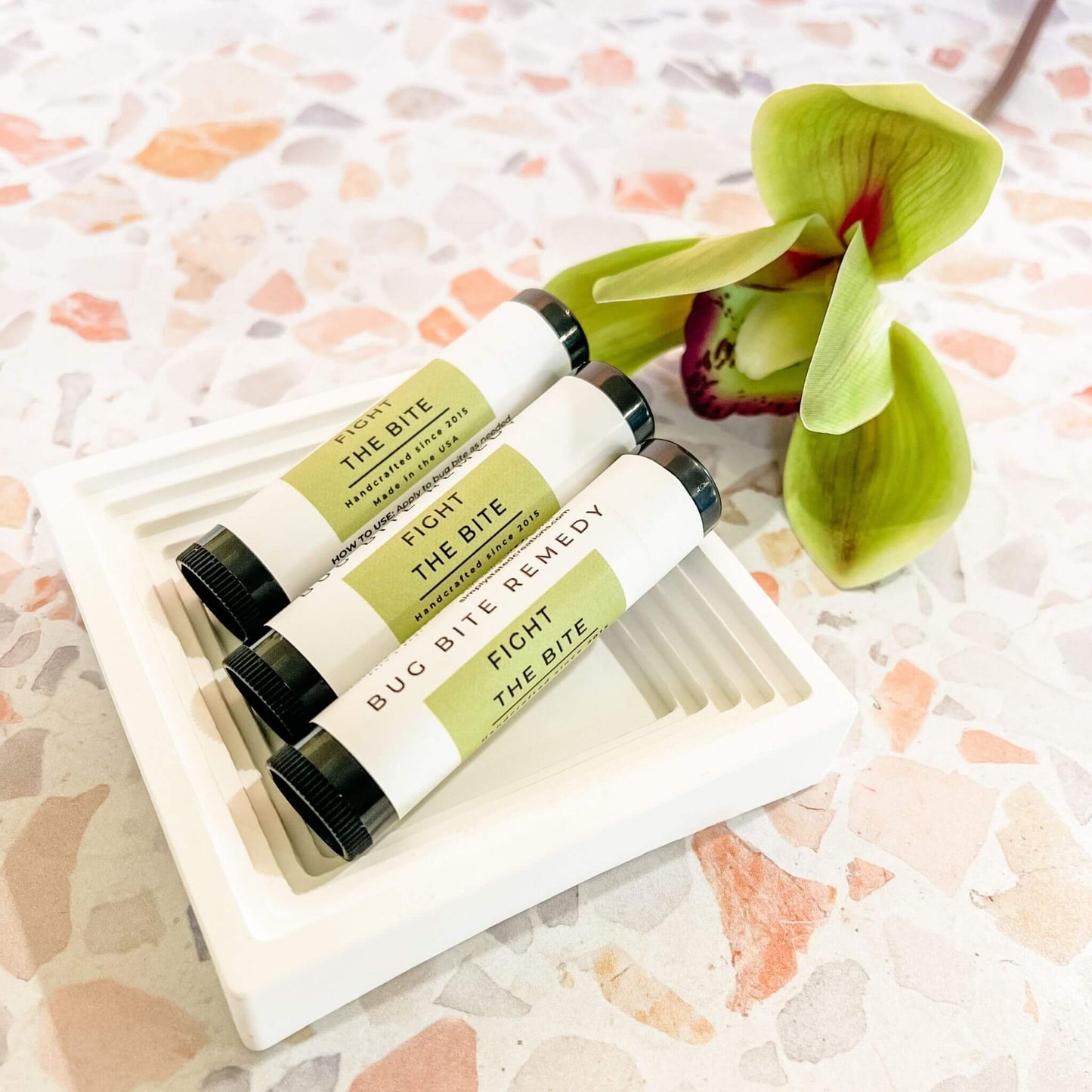 Three tubes of 'Bug Bite Remedy' on a white tray with green leaves on a patterned background
