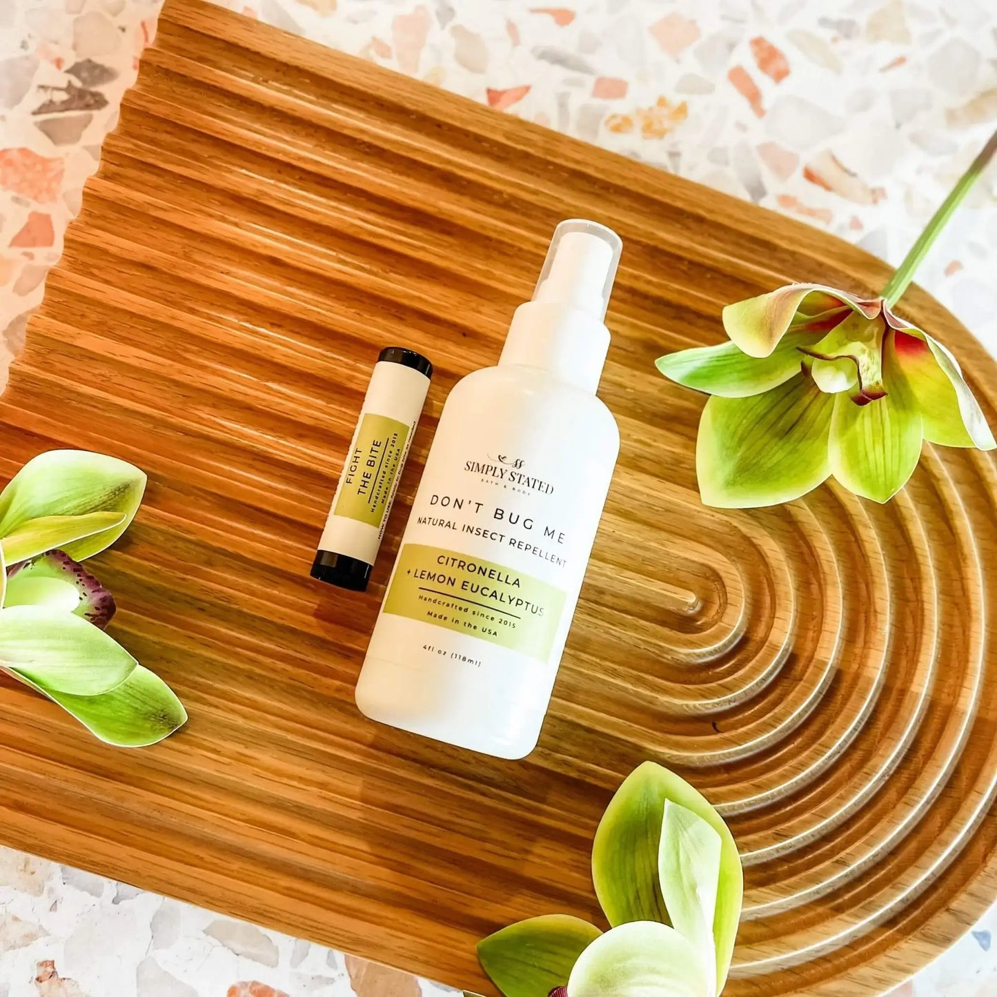 Insect repellent bottle and stick on a wooden surface with green leaves.