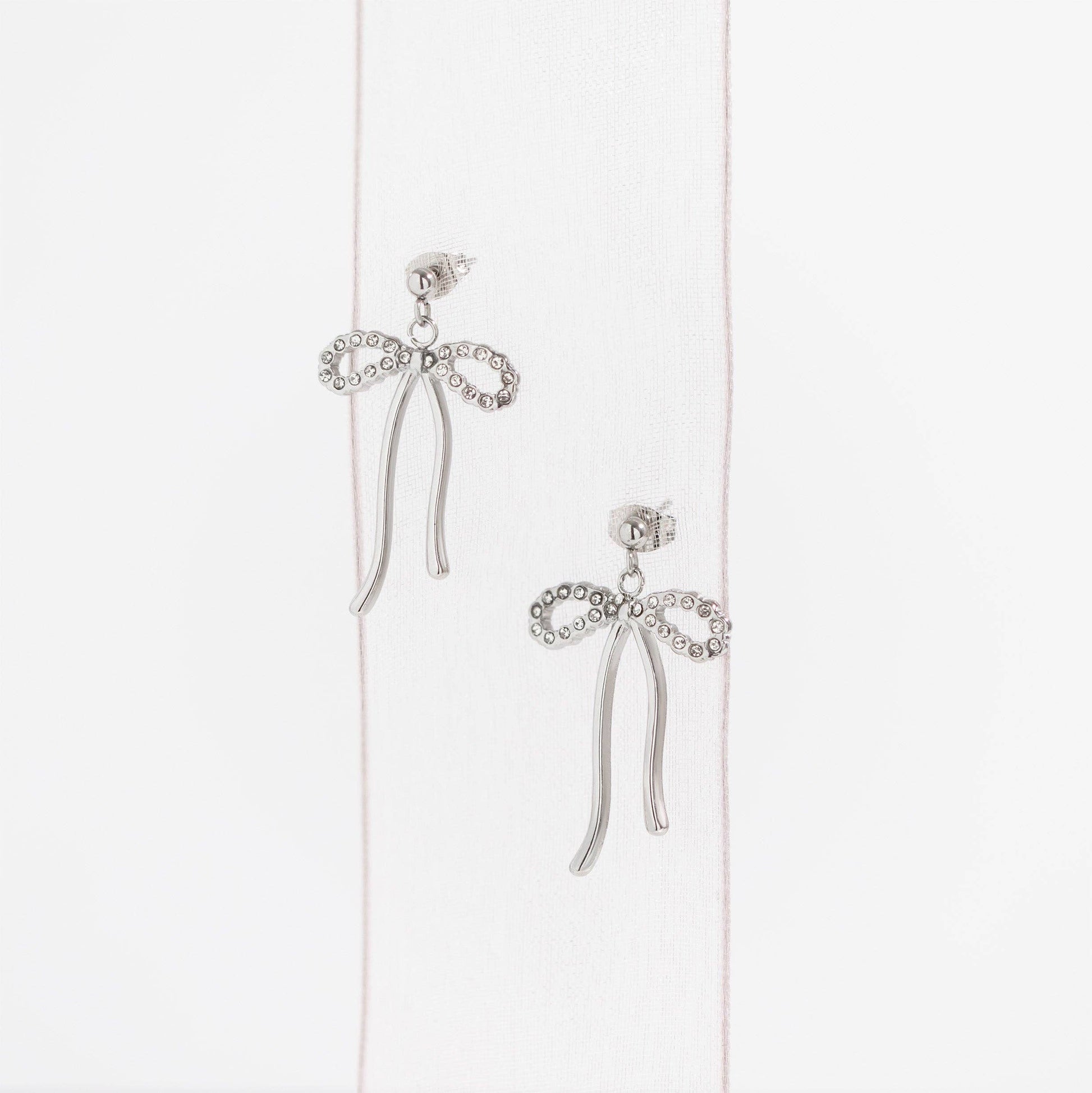 Silver bow-shaped earrings on a light pink background