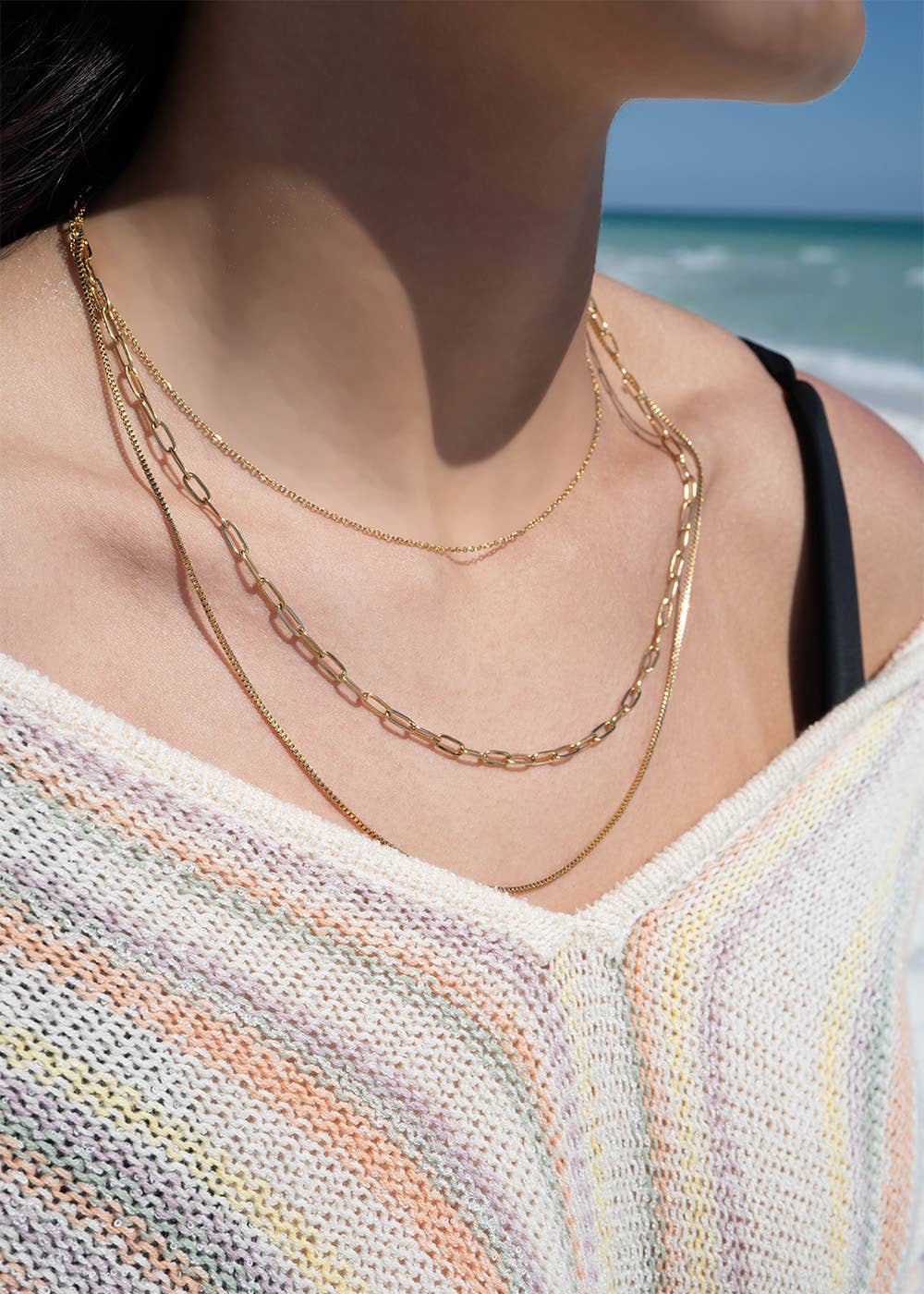 Close-up of a person wearing gold chain necklaces with a beach in the background