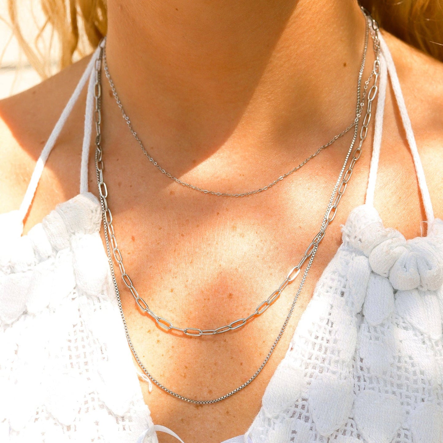 Close-up of a person wearing multiple silver necklaces with a blurred background