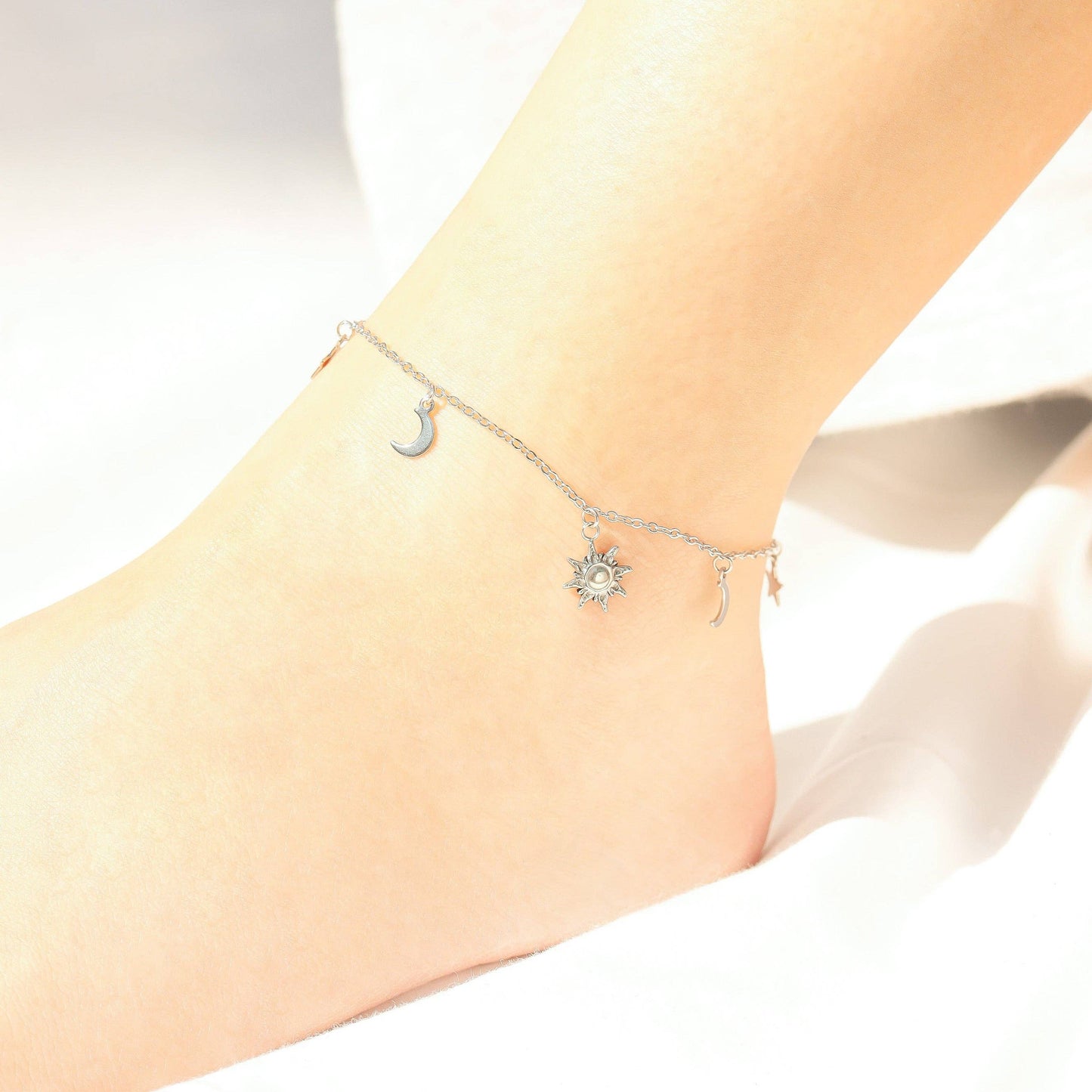 Silver anklets with moon and star designs on a person's ankle against a white background