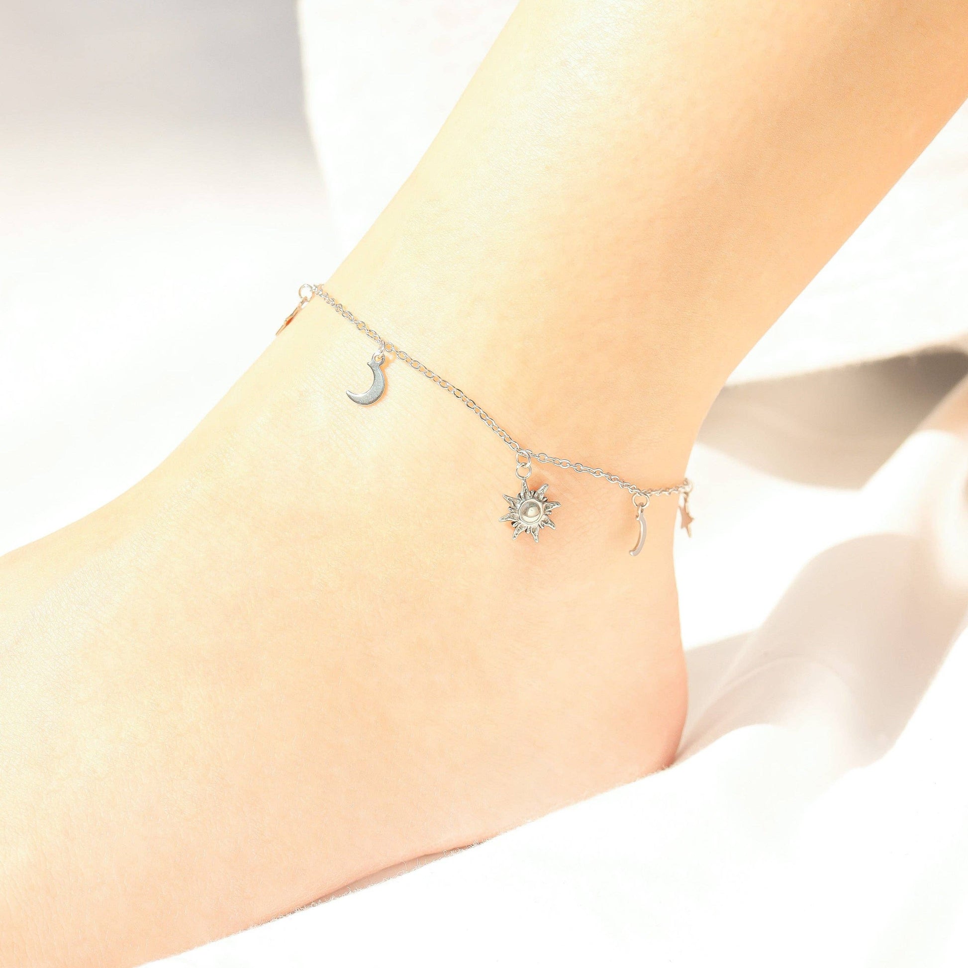 Silver anklets with moon and star designs on a person's ankle against a white background