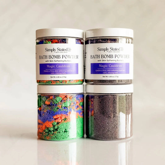 Four jars of Simply Stated Magic Cauldron bath bomb powder arranged in a 2x2 stack on a light reflective surface. The top two jars show the white powder through clear containers with white lids and white labels featuring a purple band.