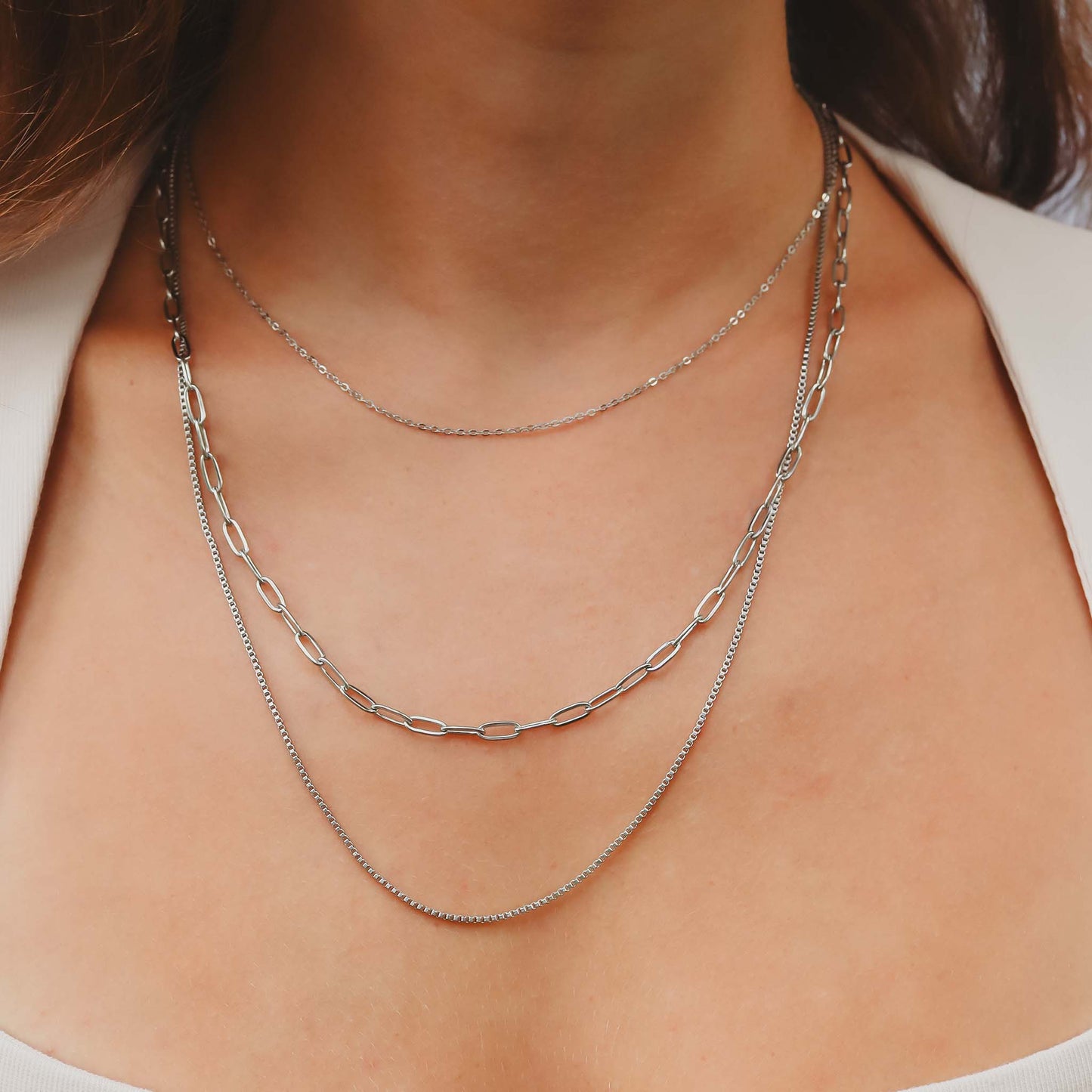 Close-up of a person wearing two silver necklaces on a plain background