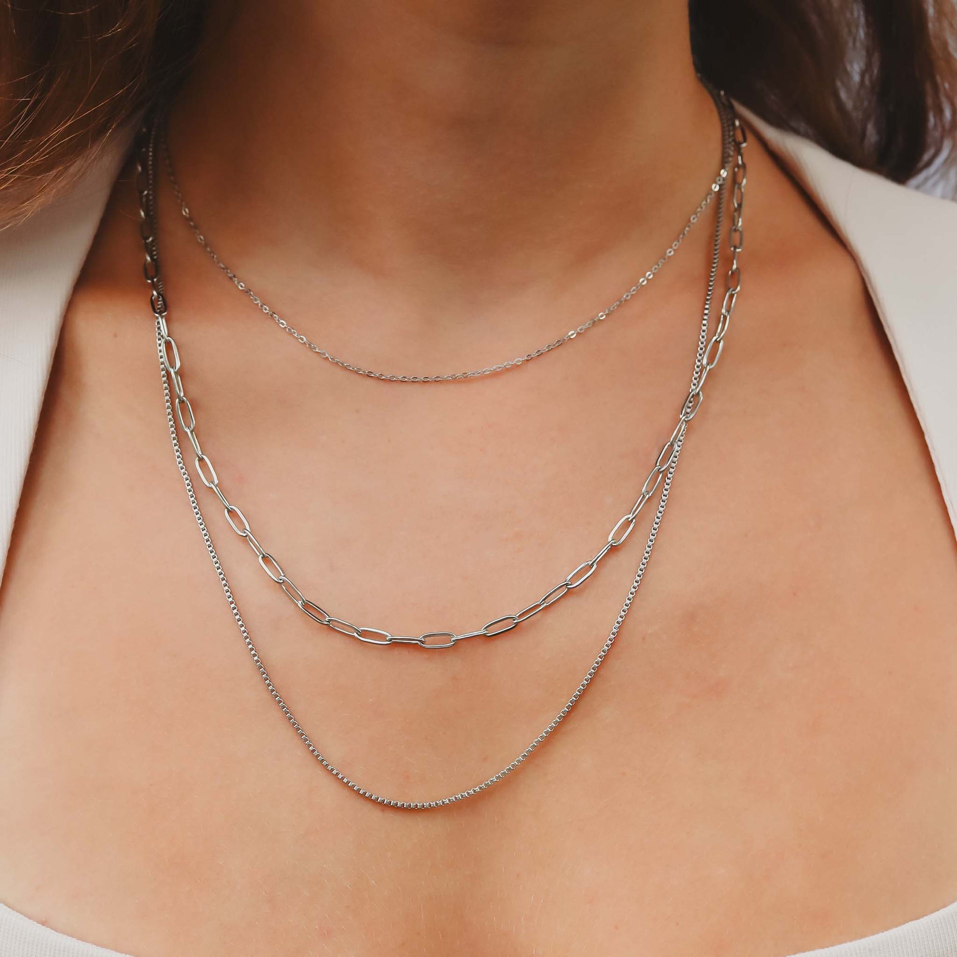 Close-up of a person wearing two silver necklaces on a plain background