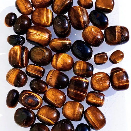A pile of polished tiger's eye gemstone beads with smooth, rounded shapes, showing their characteristic golden-brown and black banded patterns on a white background.