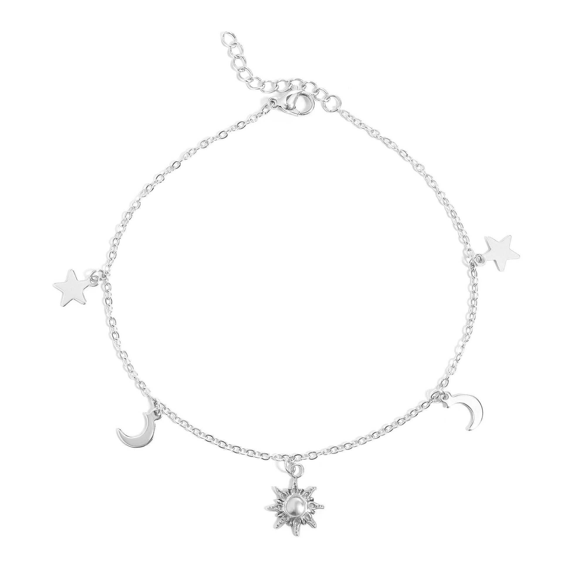 A delicate silver chain anklet featuring celestial charms, including a central sun charm with a pearl center, flanked by crescent moons and stars, shown on a plain white background.