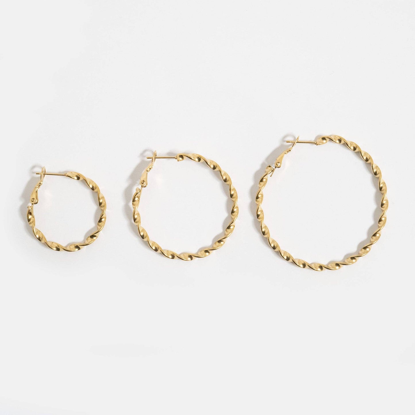 Three gold hoop earrings of different sizes on a white background