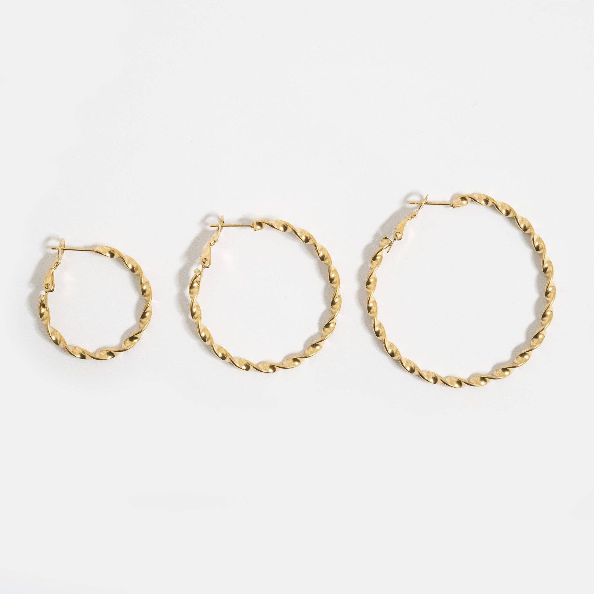 Three gold hoop earrings of different sizes on a white background