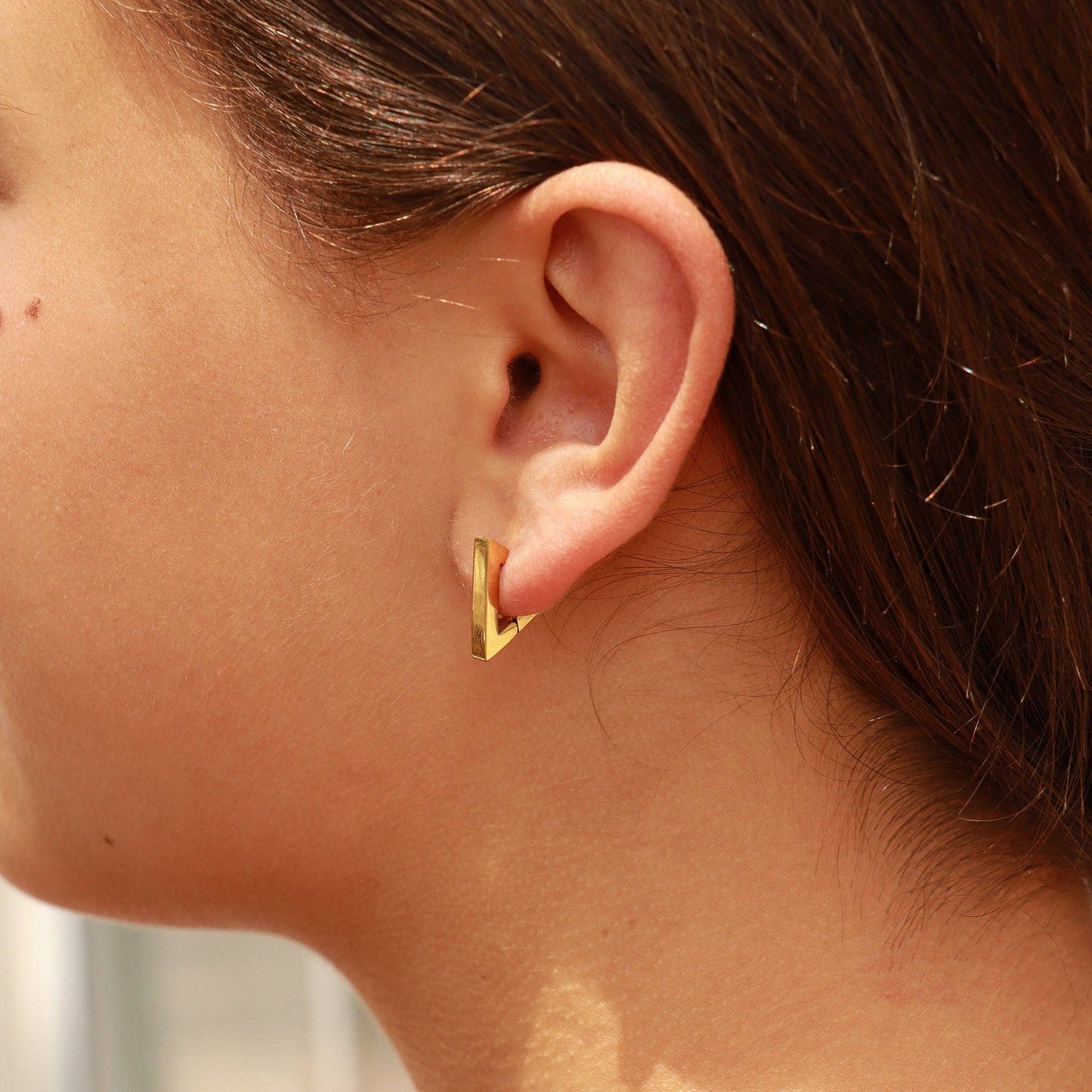 Gold geometric earring worn by a person with blurred background