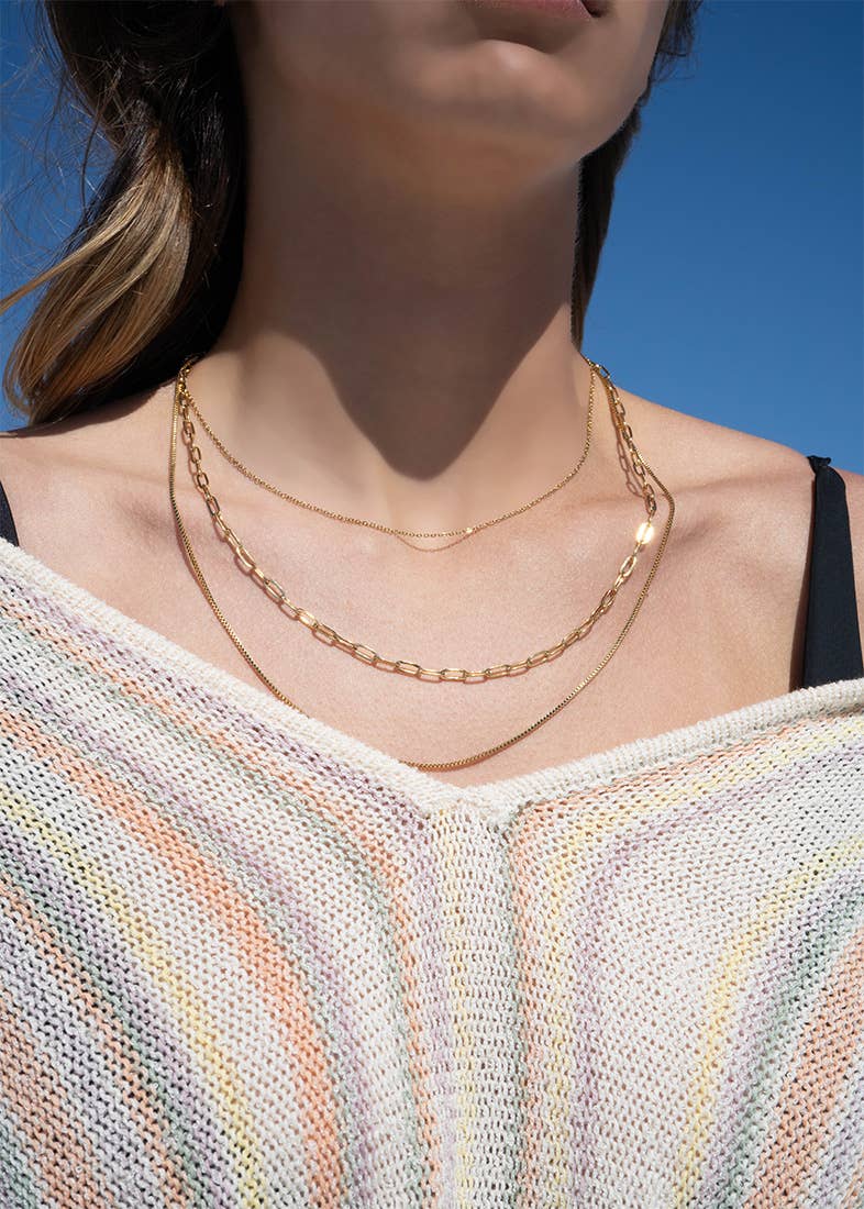 Close-up of a person wearing gold necklaces against a blue sky.